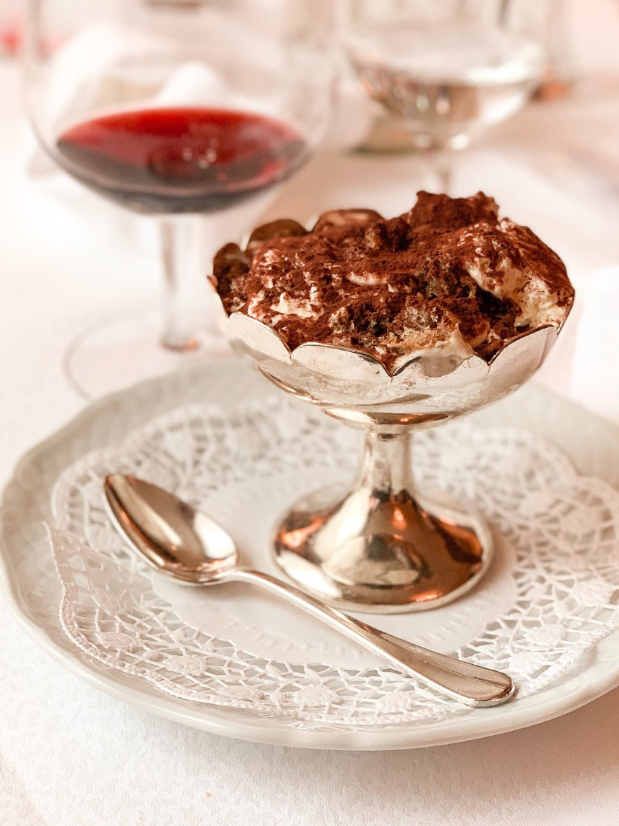 Immagine coppa di tiramisù con calice di vino rosso su tovaglia bianca